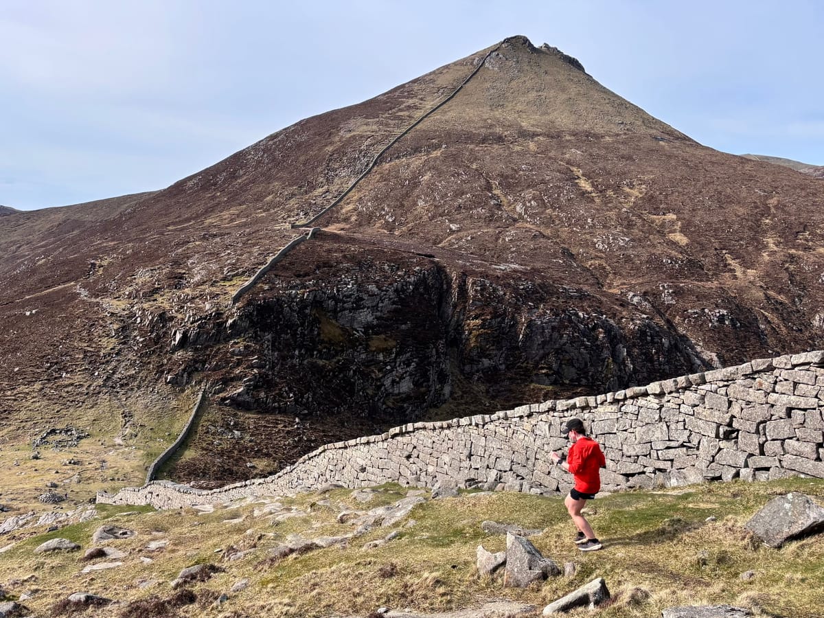 A runner in red passes the Mourne Wall as it climbs a steep, rocky Mourne peak