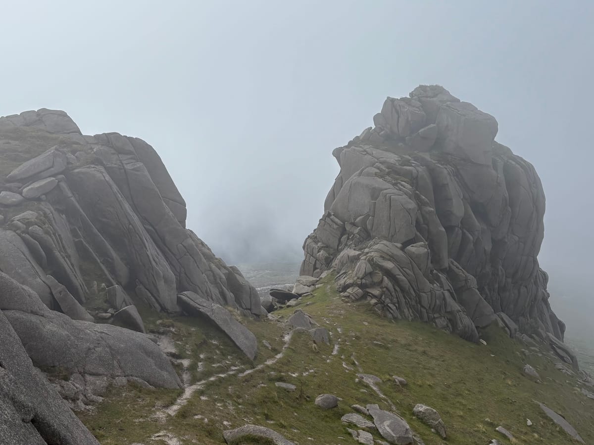 Granite tors in thick mist, with a faint path running between them and disappearing into the cloud